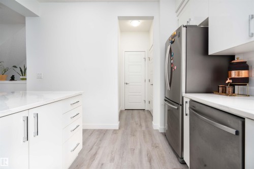 Kitchen with white cabinets, stainless steel appliances, light stone counters, and light wood finished floors - 24 2072 Wonnacott Way, Edmonton, AB - Indoor Photo Showing Kitchen