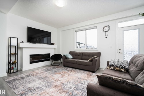 Living room featuring a glass covered fireplace, wood finished floors, and a textured ceiling - 24 2072 Wonnacott Way, Edmonton, AB - Indoor Photo Showing Living Room With Fireplace