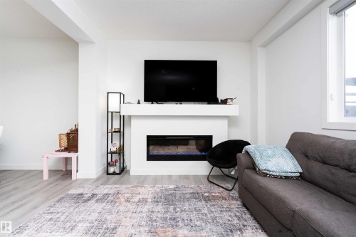 Living room featuring light wood-style floors and a glass covered fireplace - 24 2072 Wonnacott Way, Edmonton, AB - Indoor Photo Showing Living Room With Fireplace