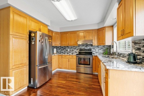 Kitchen with light stone counters, stainless steel appliances, dark wood-type flooring, backsplash, and a textured ceiling - 11608 11A Avenue, Edmonton, AB - Indoor Photo Showing Kitchen