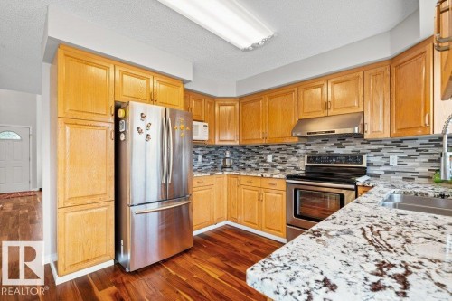Kitchen with stainless steel appliances, light stone countertops, dark wood-style flooring, backsplash, and under cabinet range hood - 11608 11A Avenue, Edmonton, AB - Indoor Photo Showing Kitchen With Double Sink