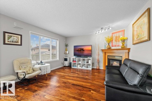 Living room featuring wood finished floors, a glass covered fireplace, and a textured ceiling - 11608 11A Avenue, Edmonton, AB - Indoor Photo Showing Living Room With Fireplace