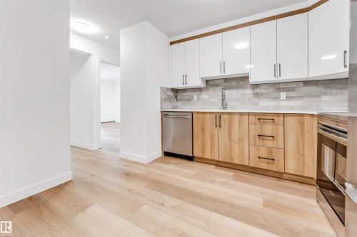 Two tone kitchen with two tone cabinets, light wood-style floors, stainless steel appliances, modern cabinets, and backsplash - 107 9760 176 St, Edmonton, AB - Indoor Photo Showing Kitchen