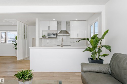 Kitchen featuring white cabinets, light wood-style flooring, backsplash, modern cabinets, and stainless steel microwave - 13520 113A Street, Edmonton, AB - Indoor