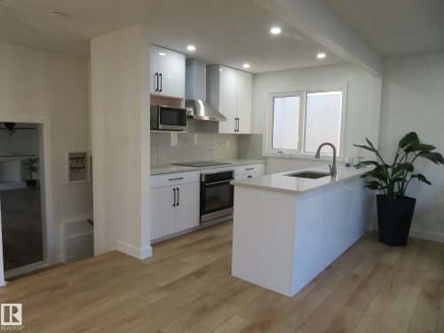Modern kitchen featuring white cabinetry, stainless steel appliances, a white island with an undermount sink, and wood-finish flooring - 13520 113A Street, Edmonton, AB - Indoor Photo Showing Kitchen With Upgraded Kitchen