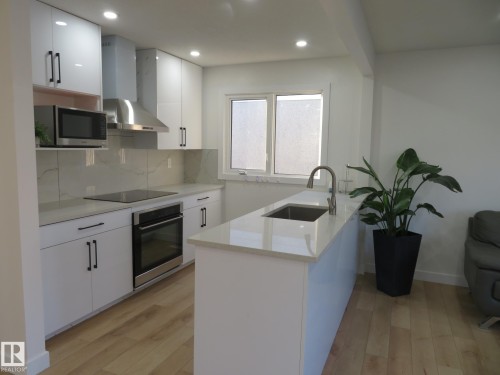 Modern kitchen featuring white cabinetry, light-toned countertops, stainless steel appliances, and wood-finish flooring - 13520 113A Street, Edmonton, AB - Indoor Photo Showing Kitchen With Upgraded Kitchen