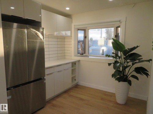 Kitchenette featuring a stainless steel refrigerator, white flat-panel cabinetry, white subway tile backsplash, and light wood-finish flooring - 13520 113A Street, Edmonton, AB - Indoor Photo Showing Other Room