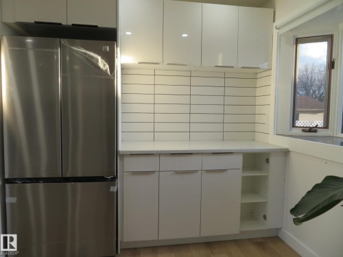 Contemporary kitchen corner featuring white flat-panel cabinetry with recessed pulls, white subway tile backsplash, and a light-toned countertop - 13520 113A Street, Edmonton, AB - Indoor