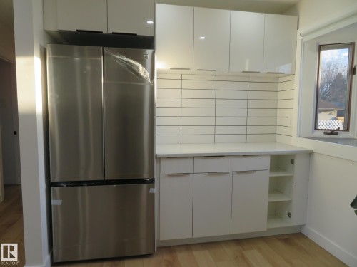 Modern kitchen area featuring a stainless steel French door refrigerator, white flat-panel cabinetry, a bright white countertop, and a tiled backsplash - 13520 113A Street, Edmonton, AB - Indoor Photo Showing Kitchen