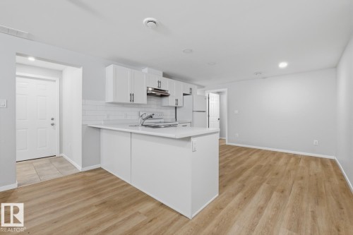 Open concept living space featuring a kitchen with white cabinetry, a light-colored countertop, and a white subway tile backsplash, alongside light wood-style flooring - 11332 134 Avenue, Edmonton, AB - Indoor Photo Showing Kitchen