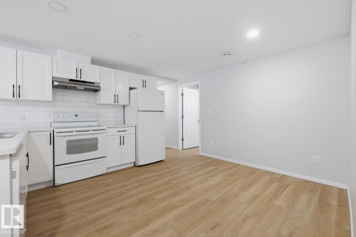 The kitchen features white cabinetry with dark hardware, a white tile backsplash, and white appliances including a stove, oven, and refrigerator - 11332 134 Avenue, Edmonton, AB - Indoor Photo Showing Kitchen With Double Sink