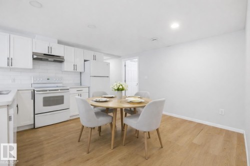 The kitchen features white cabinetry, a subway tile backsplash, and white appliances including a refrigerator, oven, and range hood - 11332 134 Avenue, Edmonton, AB - Indoor