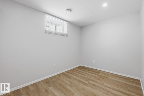 This room features light-colored walls and wood-look flooring, complemented by a window with blinds - 11332 134 Avenue, Edmonton, AB - Indoor Photo Showing Other Room