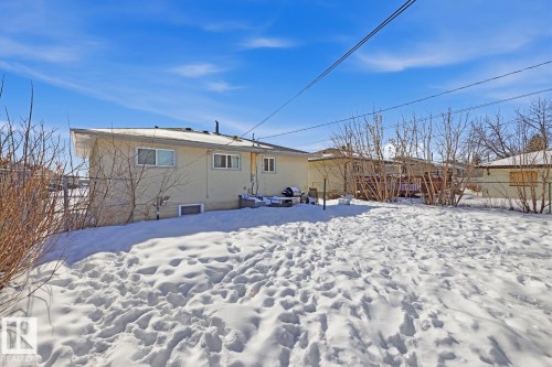 The property features a spacious rear yard with a snow-covered lawn and mature deciduous trees - 11332 134 Avenue, Edmonton, AB - Outdoor