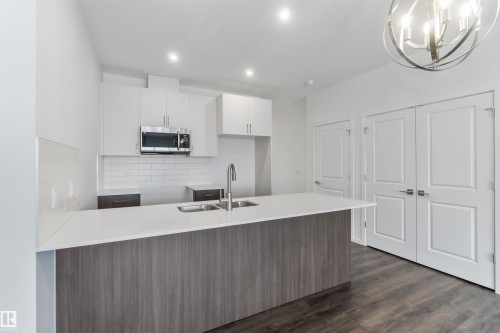 Kitchen featuring a peninsula, stainless steel microwave, white cabinets, modern cabinets, and light stone counters - 2467 Alces Link Link, Edmonton, AB - Indoor Photo Showing Kitchen With Double Sink