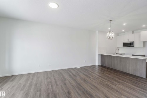Kitchen featuring white cabinets, modern cabinets, a peninsula, open floor plan, and stainless steel microwave - 2467 Alces Link Link, Edmonton, AB - Indoor Photo Showing Kitchen