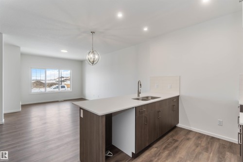 Kitchen featuring a peninsula, dark wood finish cabinets, dark wood finished floors, hanging lights, and open floor plan - 2467 Alces Link Link, Edmonton, AB - Indoor Photo Showing Kitchen With Double Sink