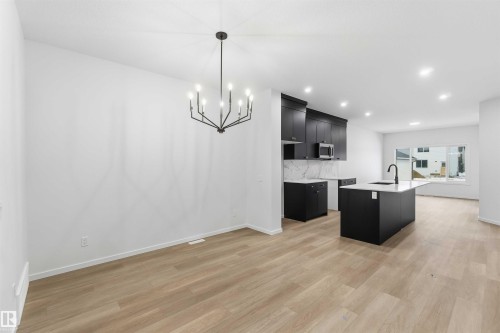 Kitchen with dark cabinets, a kitchen island with sink, light wood-style floors, suspended lighting, and light stone countertops - 8652 Edgemont Link Link, Edmonton, AB - Indoor Photo Showing Kitchen With Upgraded Kitchen
