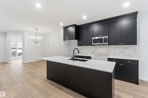 Kitchen featuring an island with sink, dark cabinets, stainless steel microwave, hanging lights, and light stone counters - 8652 Edgemont Link Link, Edmonton, AB - Indoor Photo Showing Kitchen With Double Sink With Upgraded Kitchen