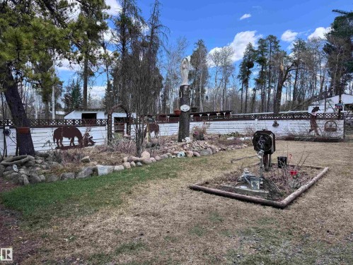 Expansive outdoor space featuring a white privacy fence with decorative metal cutouts, mature trees, and a landscaped garden bed with natural stone accents - 59415A Rg Rd 240, Rural Westlock County, AB - Outdoor