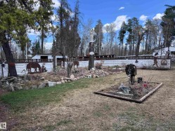 Expansive outdoor space featuring a white privacy fence with decorative metal cutouts, mature trees, and a landscaped garden bed with natural stone accents - 