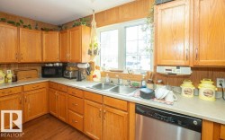 Kitchen with dishwasher, light countertops, black microwave, dark wood-type flooring, and wood finish cabinetry - 