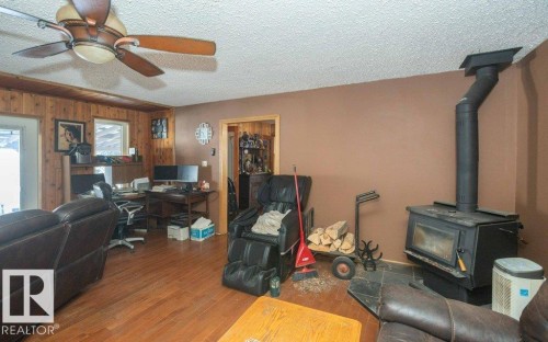 Office area with wooden walls, wood finished floors, a textured ceiling, a wood stove, and ceiling fan - 59415A Rg Rd 240, Rural Westlock County, AB - Indoor With Fireplace