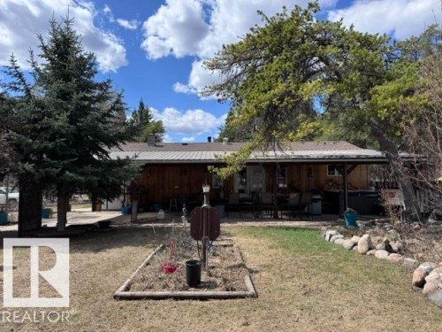 Wood-sided exterior featuring a covered patio, a metal roof, and an expansive lawn area - 59415A Rg Rd 240, Rural Westlock County, AB - Outdoor