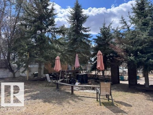 Fenced backyard featuring mature evergreen trees, a built-in wooden bench, and a gravel ground cover - 59415A Rg Rd 240, Rural Westlock County, AB - Outdoor