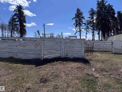 White-painted wooden fencing featuring a walk-through gate and a metal panel gate, bordered by mature evergreen trees - 59415A Rg Rd 240, Rural Westlock County, AB - Outdoor With View