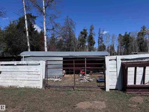 Corrugated metal outbuilding featuring an open-faced shelter and an enclosed storage area, surrounded by a white horizontal plank fence and a wire gate - 59415A Rg Rd 240, Rural Westlock County, AB - Outdoor