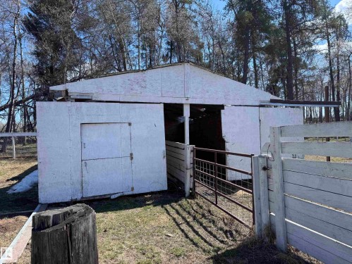 White outbuilding with a peaked roof, featuring a hinged door and an open entrance, bordered by a white wooden fence and a metal gate - 59415A Rg Rd 240, Rural Westlock County, AB - Outdoor