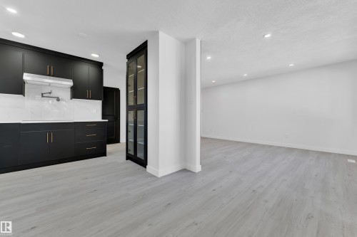 Kitchen featuring dark cabinetry, recessed lighting, light wood-style floors, glass fronted cabinets, and decorative backsplash - 8635 33 Avenue, Edmonton, AB - Indoor Photo Showing Kitchen