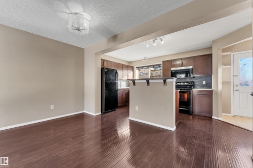 Kitchen with black appliances, a kitchen bar, dark wood-style flooring, a textured ceiling, and a kitchen island - 6017 213 Street, Edmonton, AB - Indoor Photo Showing Kitchen