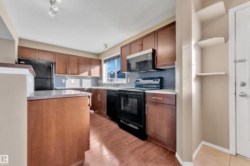 Kitchen with black appliances, light countertops, decorative backsplash, a textured ceiling, and light wood finished floors - 6017 213 Street, Edmonton, AB - Indoor Photo Showing Kitchen