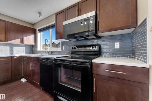 Kitchen with black appliances, dark wood-type flooring, decorative backsplash, light stone countertops, and dark wood finish cabinetry - 6017 213 Street, Edmonton, AB - Indoor Photo Showing Kitchen
