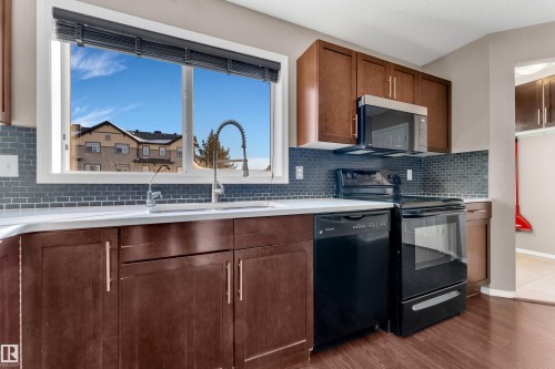 Kitchen featuring black appliances, wood finish cabinetry, dark wood-style floors, and light stone countertops - 6017 213 Street, Edmonton, AB - Indoor Photo Showing Kitchen With Double Sink