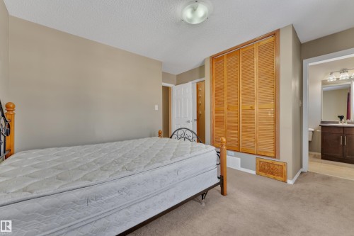 Bedroom with light colored carpet, a closet, a textured ceiling, and ensuite bathroom - 6017 213 Street, Edmonton, AB - Indoor Photo Showing Bedroom