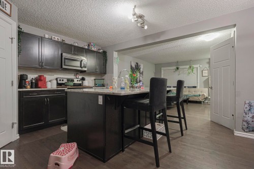 Kitchen featuring dark cabinets, dark wood-style floors, a kitchen island with sink, a breakfast bar area, and a textured ceiling - 21971 91 Avenue Nw, Edmonton, AB - Indoor