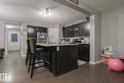 Kitchen featuring dark wood-style floors, a breakfast bar area, a kitchen island, stainless steel appliances, and a textured ceiling - 21971 91 Avenue Nw, Edmonton, AB - Indoor