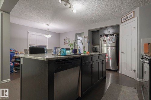 Kitchen featuring stainless steel appliances, a center island with sink, dark wood finished floors, light stone countertops, and a textured ceiling - 21971 91 Avenue Nw, Edmonton, AB - Indoor Photo Showing Kitchen