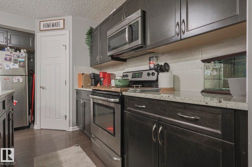 Kitchen featuring stainless steel appliances, a textured ceiling, dark wood-type flooring, and light stone countertops - 21971 91 Avenue Nw, Edmonton, AB - Indoor Photo Showing Kitchen