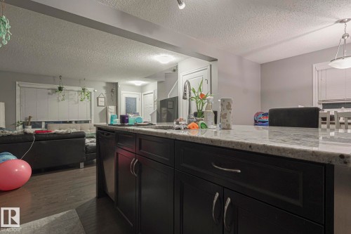 Kitchen featuring open floor plan, dark cabinetry, hanging light fixtures, light stone counters, and a textured ceiling - 21971 91 Avenue Nw, Edmonton, AB - Indoor Photo Showing Bathroom