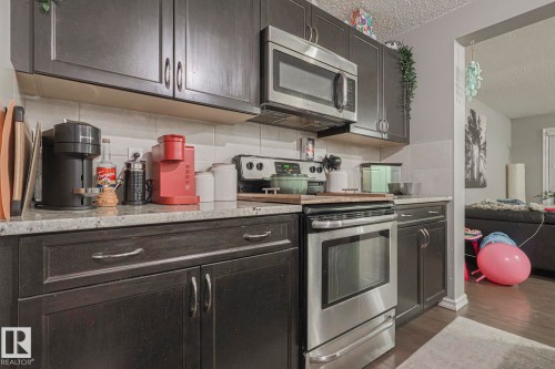 Kitchen featuring stainless steel appliances, a textured ceiling, dark wood finish cabinets, dark wood-style flooring, and light stone countertops - 21971 91 Avenue Nw, Edmonton, AB - Indoor Photo Showing Kitchen