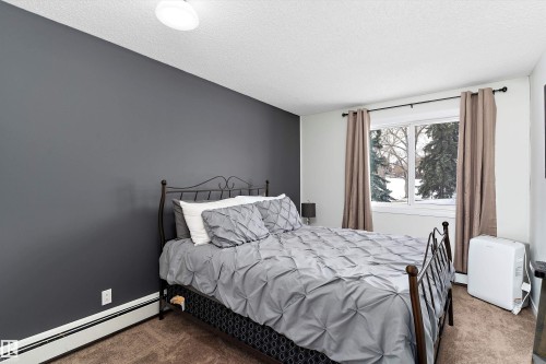 Carpeted bedroom featuring a baseboard heating unit and a textured ceiling - # 3 13450 Fort Road, Edmonton, AB - Indoor Photo Showing Bedroom