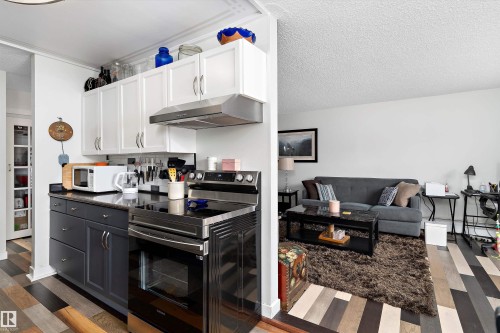 Kitchen featuring stainless steel range with electric stovetop, exhaust hood, white cabinets, a textured ceiling, and dark wood-style flooring - # 3 13450 Fort Road, Edmonton, AB - Indoor Photo Showing Kitchen