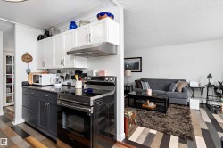 Kitchen featuring stainless steel range with electric stovetop, exhaust hood, white cabinets, a textured ceiling, and dark wood-style flooring - 