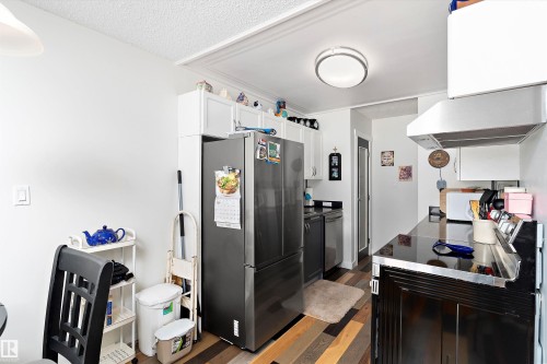 Kitchen with appliances with stainless steel finishes, wood finished floors, exhaust hood, white cabinets, and a textured ceiling - # 3 13450 Fort Road, Edmonton, AB - Indoor