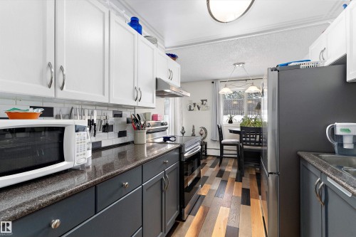 Kitchen featuring appliances with stainless steel finishes, wood finished floors, backsplash, white cabinets, and a textured ceiling - # 3 13450 Fort Road, Edmonton, AB - Indoor Photo Showing Kitchen