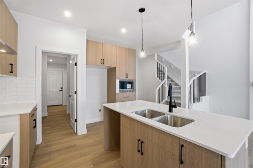 Kitchen featuring light stone counters, modern cabinets, pendant lighting, light wood finished floors, and an island with sink - 19348 29 Avenue, Edmonton, AB - Indoor Photo Showing Kitchen With Double Sink